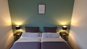 Una cama doble con dos almohadas, un objeto enmarcado en la pared y dos lámparas de noche.