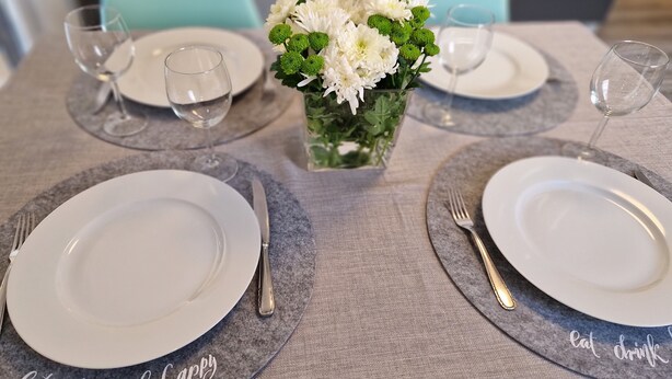 Una mesa dispuesta con platos blancos, cubiertos y copas de vino, adornada con un florero de flores blancas.