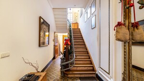 Un corridoio con piastrelle a motivi decorativi, una scala in legno, uno specchio con cornice ornata e un tavolino con una macchina da scrivere.