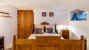 Un letto di legno con due cuscini, un comodino, un armadio di legno e una finestra con la lettera 'A' sulla parete.