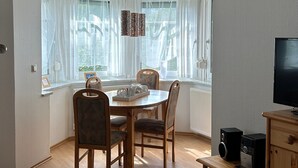 A room with a dining table, chairs, a TV, and a shelf with books. - Studio Apartment 'Wohnung 1' with Private Terrace and Wi-Fi (Oberhof)