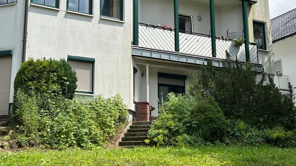 Een gebouw met twee verdiepingen, een balkon, een voordeur en een kleine trap naar de ingang.