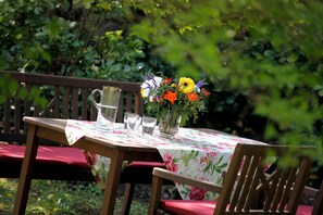 A wooden table with a floral tablecloth, a pitcher, and glasses, set outdoors with a bench and chairs. - Apartment Mattenweg - Appartement 1 - 'Gustav Klimt' (Hinterzarten)
