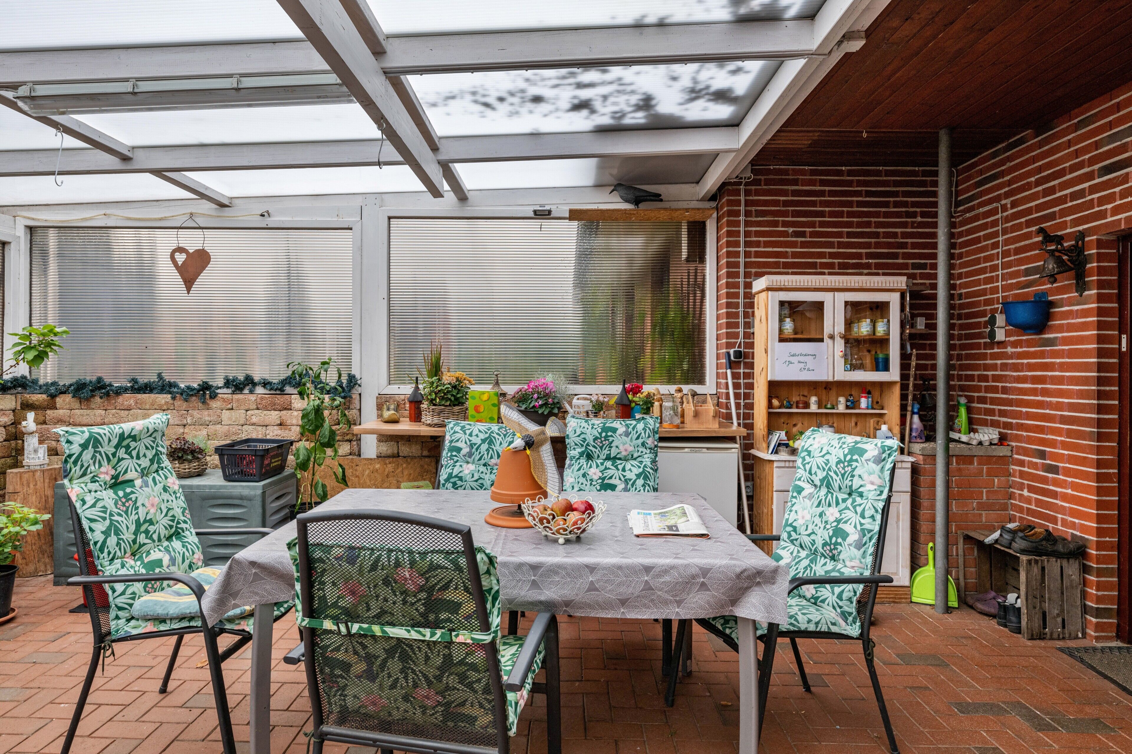 A covered patio area with a table and chairs, a brick wall, and a wooden cabinet.