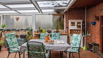 A covered patio area with a table and chairs, a brick wall, and a wooden cabinet.