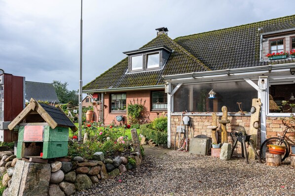 Una casa con techo inclinado, un jardín con diversas plantas y un comedero de pájaros de madera.