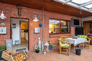 Ein Backsteinhaus mit einer Terrasse, ausgestattet mit einem Tisch, Stühlen und einem an der Wand befestigten Fernseher sowie einer Holztür.