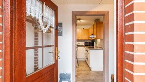 Un pasillo que conduce a una cocina con armarios de madera, un microondas y un taburete azul pequeño.
