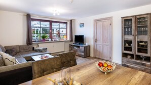 Una sala de estar con un sofá, una mesa de comedor con un frutero, un televisor y un aparador con cristalería.