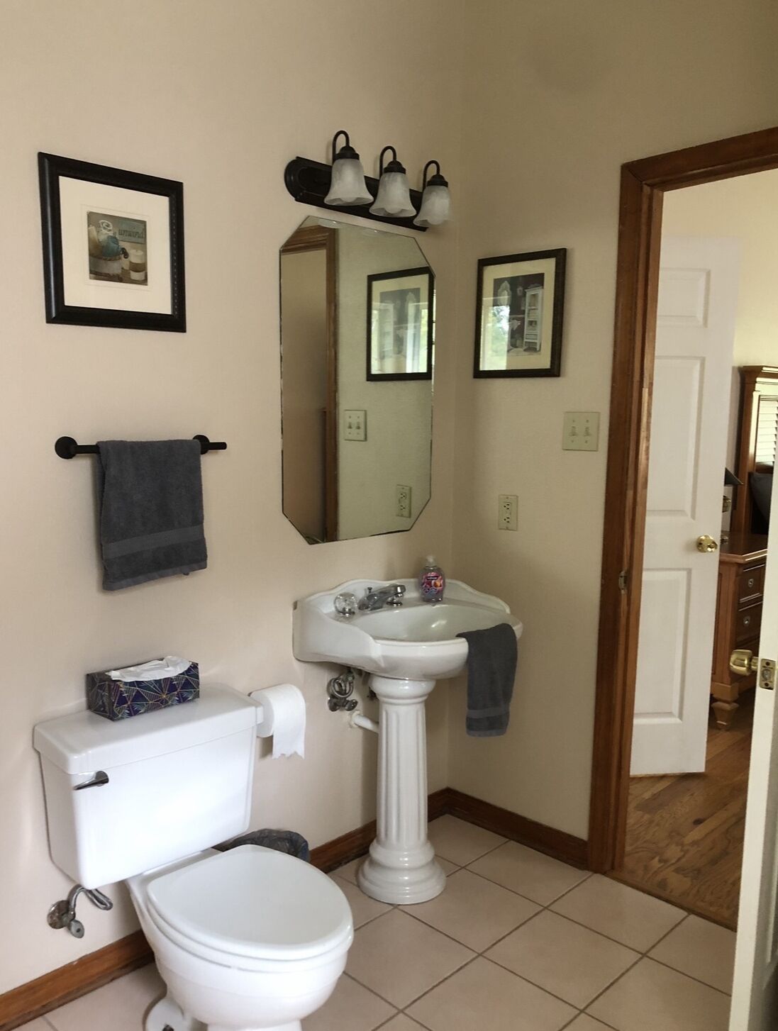 Une salle de bain avec des toilettes, un lavabo et un miroir. Des tableaux encadrés ornent le mur, et il y a un porte-serviettes.
