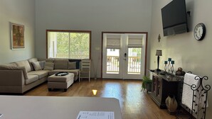 Ein Wohnzimmer mit einer Couch, einem Hocker und einem an der Wand befestigten Flachbildfernseher.