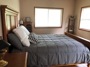 Un dormitorio con cama, mesita de noche, lámpara, ventana y estante con objetos decorativos.