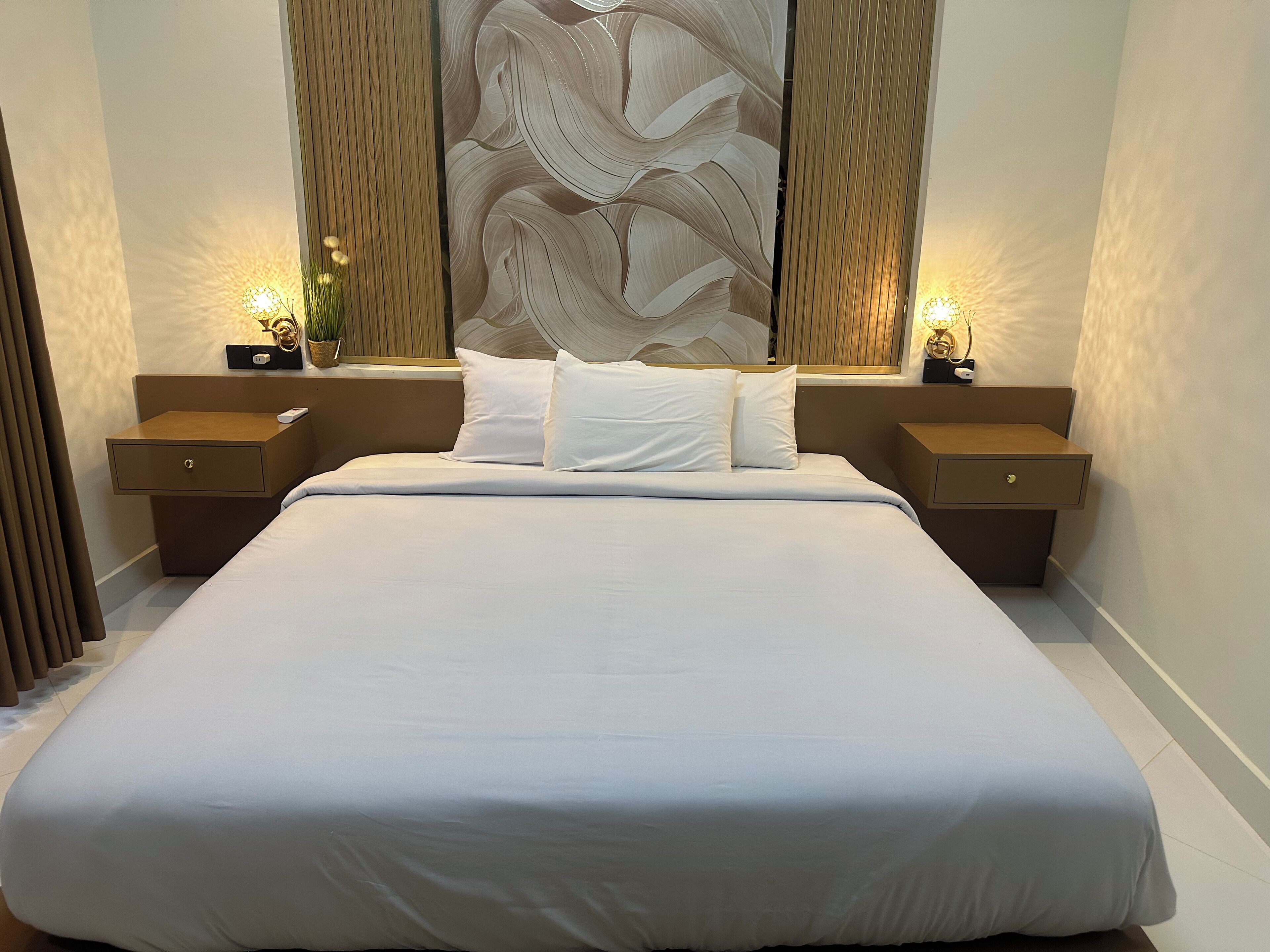 Una cama grande con sábanas blancas, dos mesitas de noche con lámparas y un panel decorativo en la pared.