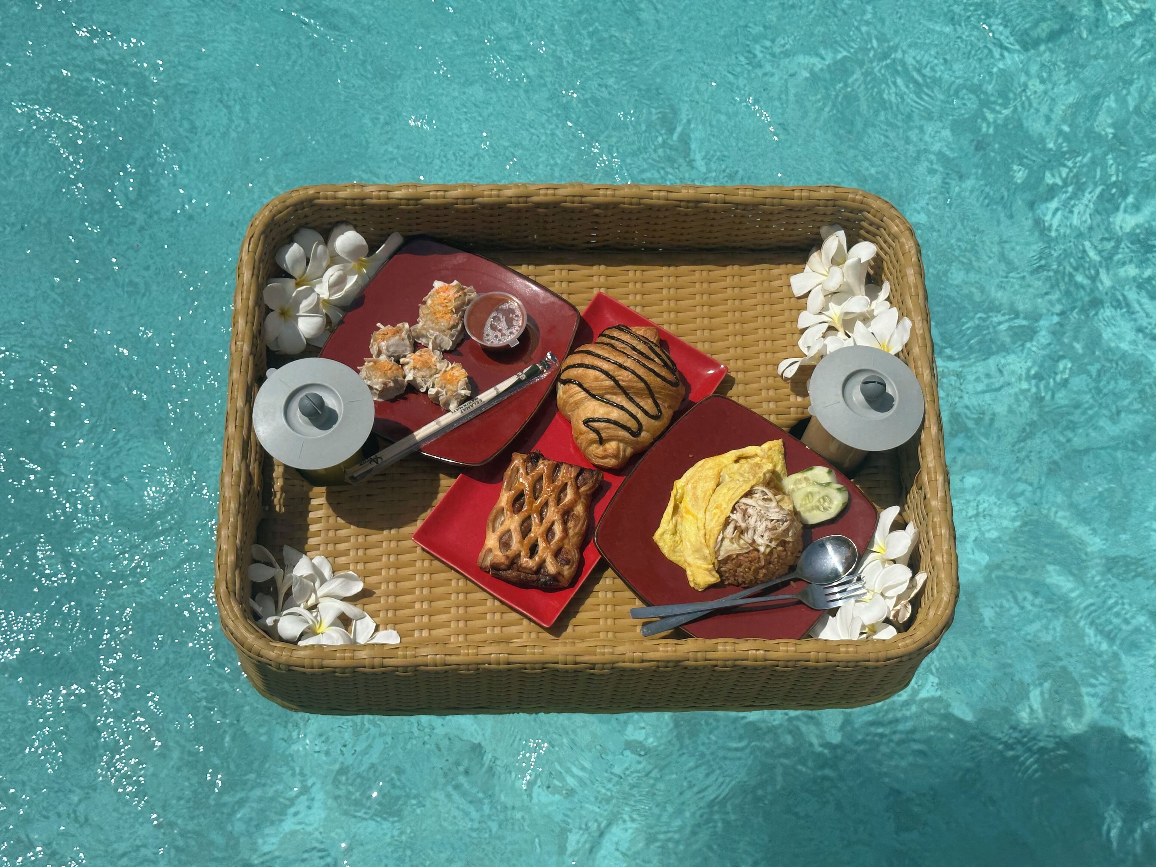 Un plateau contenant des aliments et une boisson, posé sur une table en osier près d’une piscine.