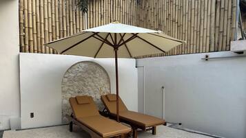 Un petit espace extérieur aménagé avec deux fauteuils et un grand parasol.