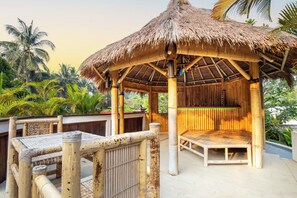 A bamboo structure with a thatched roof, surrounded by lush greenery. - Ombe Villa (Aikmel)