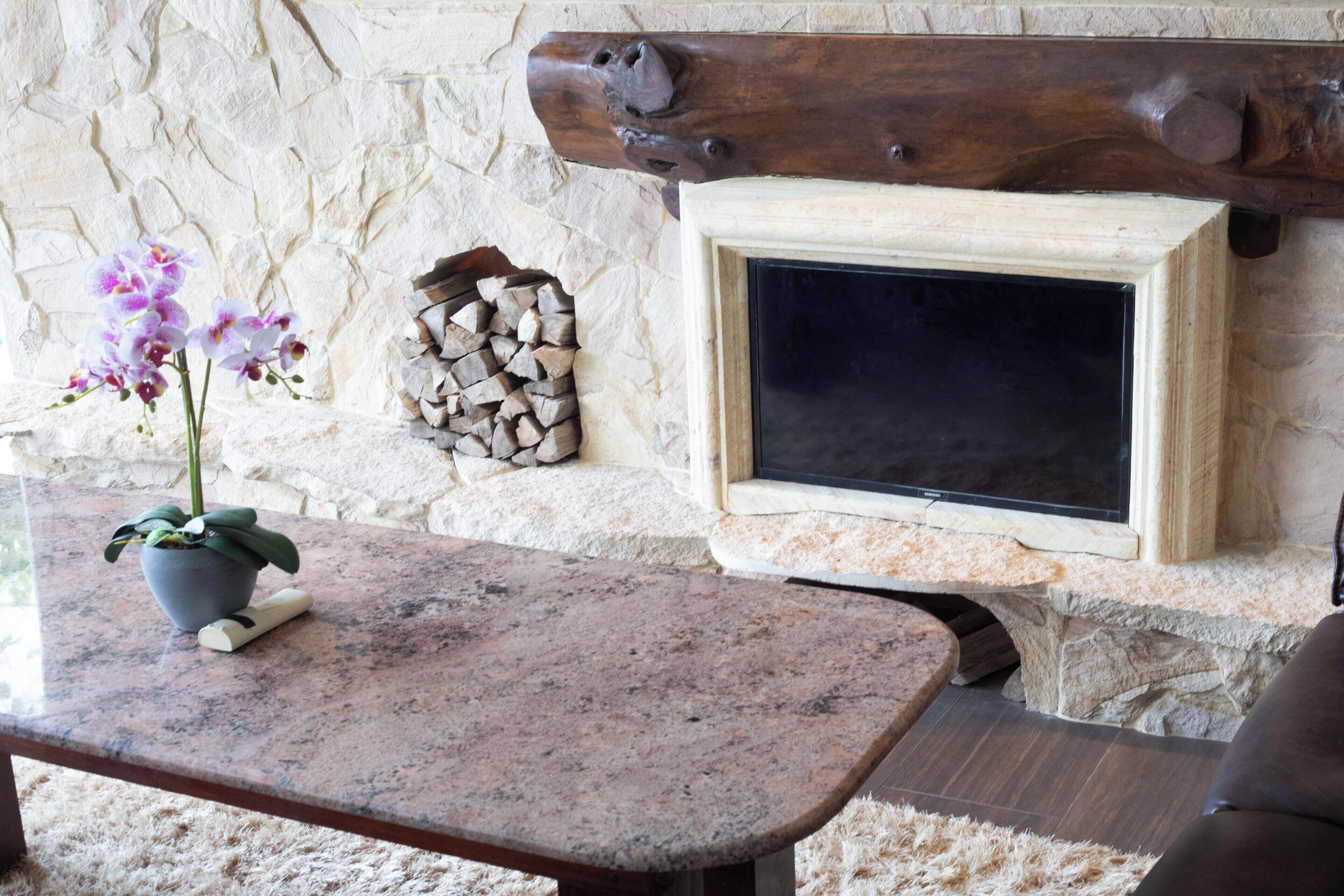 Une cheminée en pierre avec un téléviseur, une pile de bûches et une orchidée en pot sur une table en marbre.