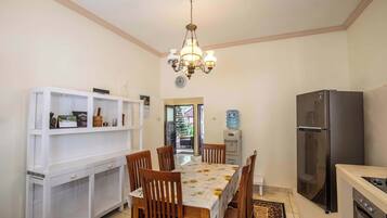 A dining area with a table set for six, surrounded by wooden chairs. A white console table with shelves is to the left, and a black refrigerator is to the right.