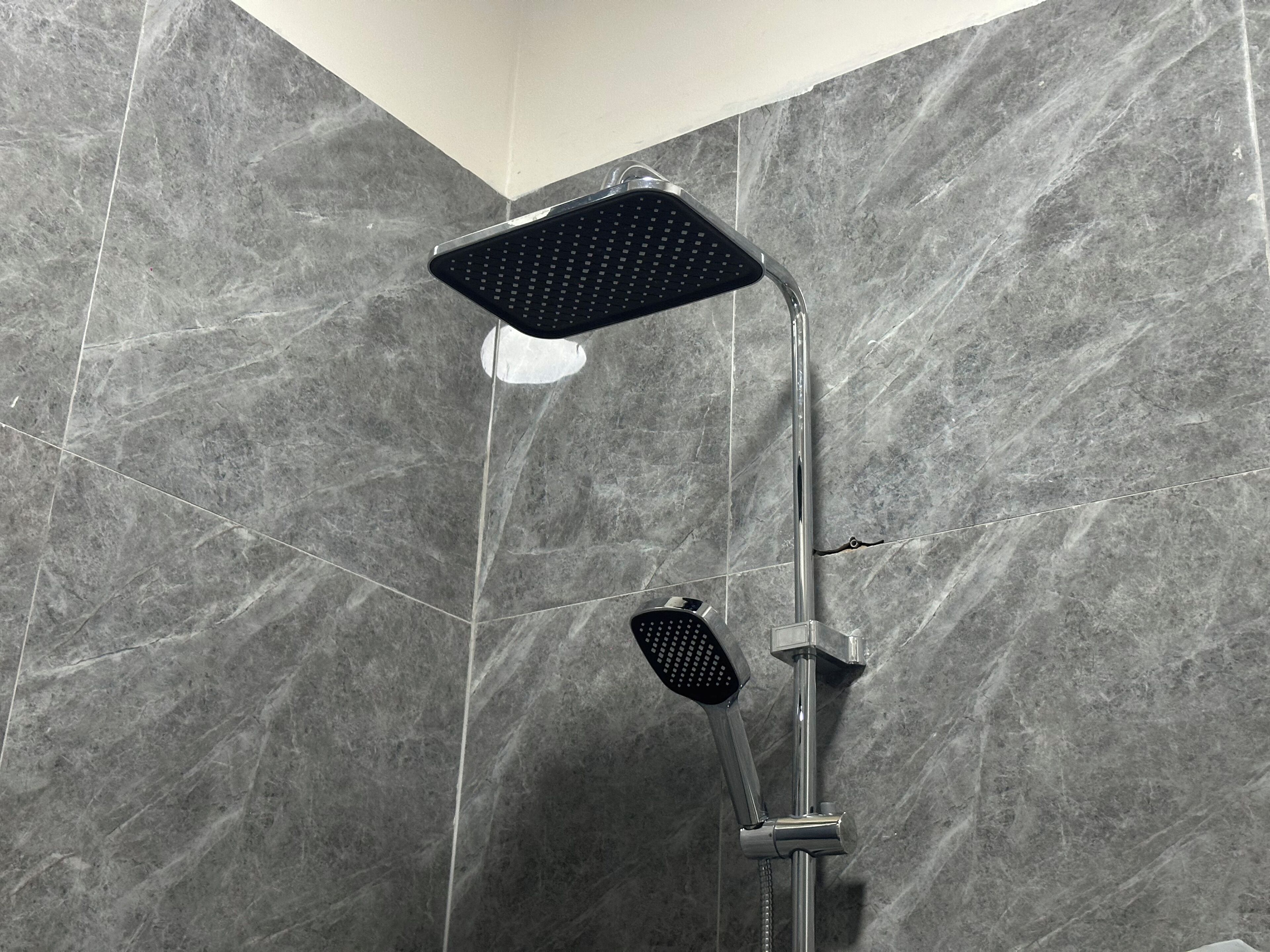 A shower with a square head and a handheld showerhead, set against a tiled wall.