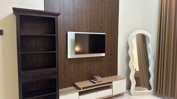 A modern living room with a TV mounted on a wooden panel wall, a large mirror, and a dark wooden cabinet.