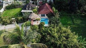 An aerial view of a residential area with houses, a swimming pool, and lush greenery. - Ombe Villa (Aikmel)