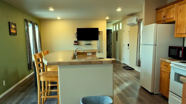 A compact kitchen with a dining area, wooden cabinets, a refrigerator, microwave, and a trash bin. - Quiet Mountain Getaway (Hesperus)