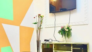A room with a flat-screen TV mounted on the wall, a vase with flowers on a shelf, and geometric wall decorations. - 1 Bed Studio Sleeps 2 - Canal View, Parking, Wifi (Douala)