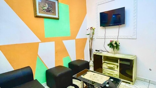 A living room with a sofa set, a coffee table, a TV, and a decorative wall. - 1 Bed Studio Sleeps 2 - Canal View, Parking, Wifi (Douala)