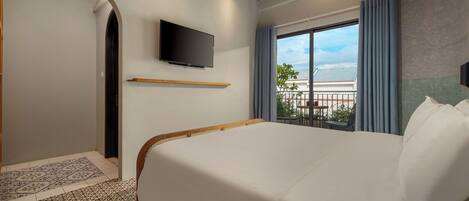 Une chambre d’hôtel avec un grand lit, un téléviseur fixé au mur, un balcon avec vue sur la mer et des carreaux de sol à motifs.