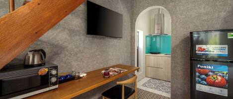 Una cocina compacta con una mesa de madera, un refrigerador negro, un microondas y un televisor montado en la pared.