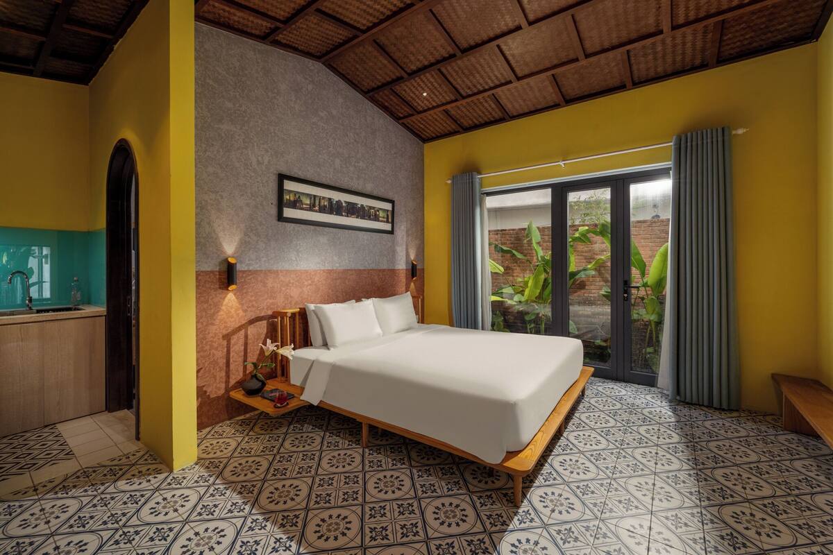 A bedroom with a bed, a nightstand, a framed picture on the wall, and a view of the outdoors through a sliding door.