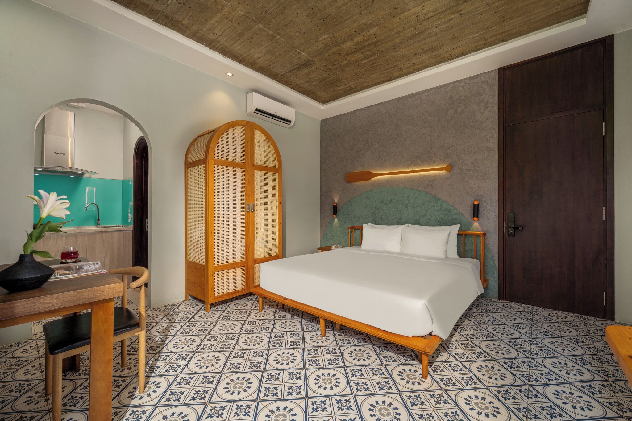 Une chambre avec un grand lit, un bureau en bois avec une chaise, une armoire et une salle de bain visible à travers une arche.