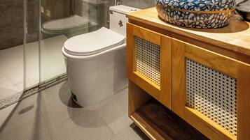 A modern bathroom with a glass-enclosed shower, a white toilet, a wooden vanity with a decorative sink, and a round mirror.