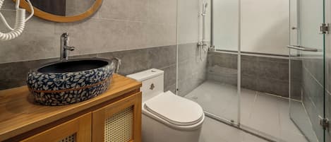 A modern bathroom with a round mirror, a patterned sink, a toilet, and a glass-enclosed shower.