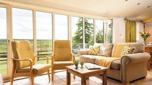 A spacious living room with large windows, a sofa, two armchairs, and a wooden coffee table. - Riverside Cottage at Grindon Farm (Hexham)