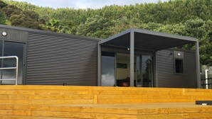 Una cabaña moderna con terraza de madera, ventanas amplias y vistas a una ladera boscosa.