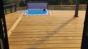 Terraza de madera con un jacuzzi y vista al mar.