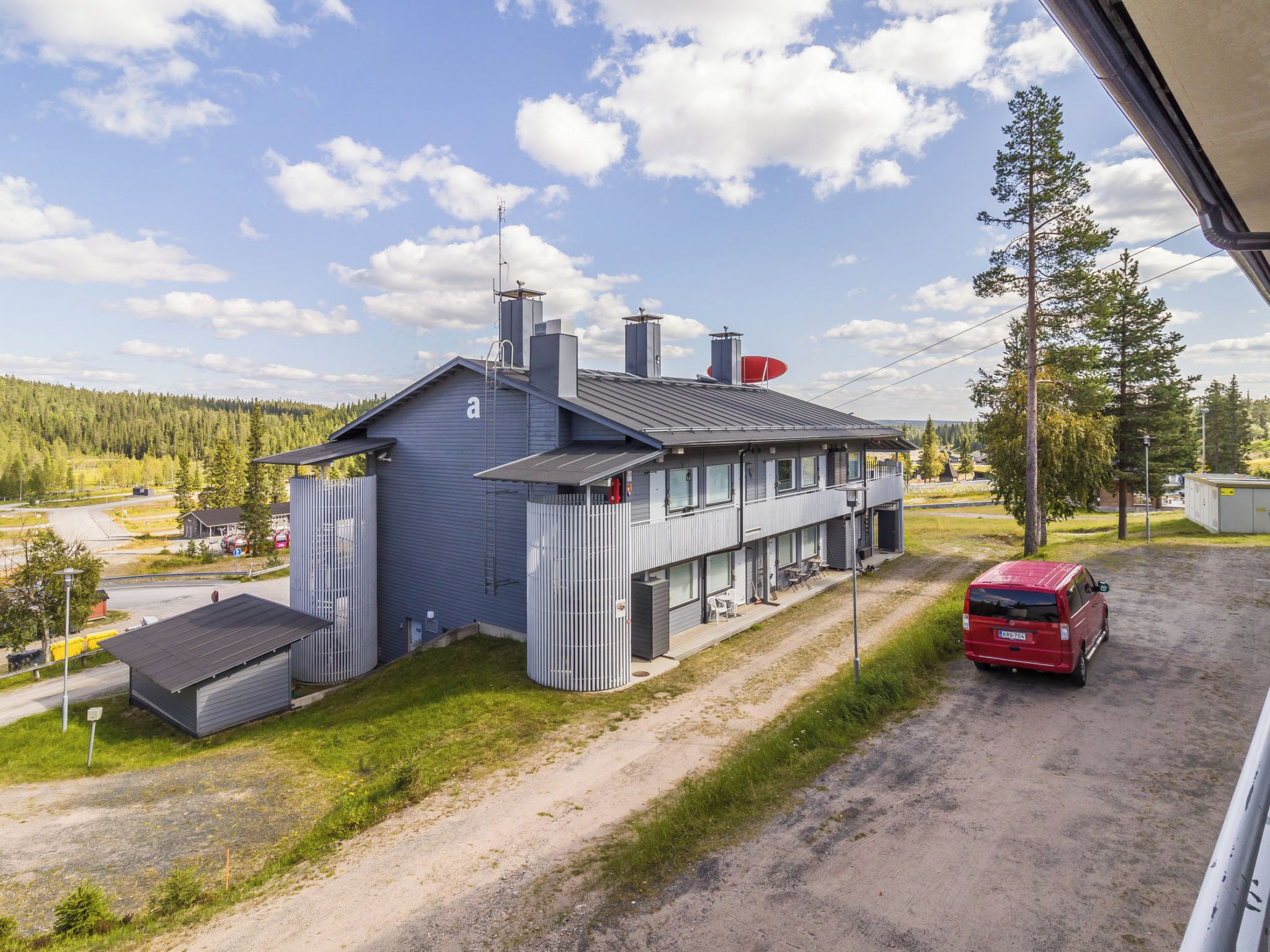 Un bâtiment à deux étages, doté d’un toit plat, d’une antenne parabolique et d’un véhicule rouge garé devant.