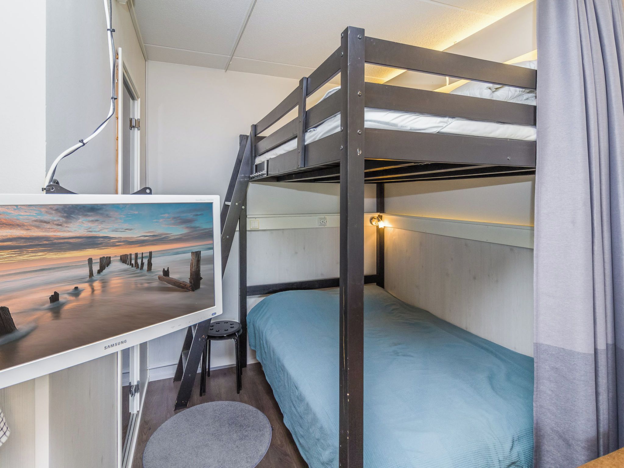 Une chambre avec un lit superposé, un bureau et un écran d’ordinateur affichant une image de paysage.