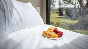 Una cama con sábanas blancas, un plato con croissants y fresas, y una vista de un área verde a través de una ventana.