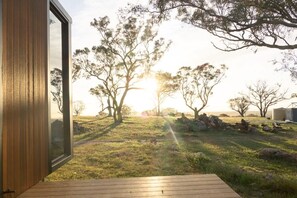 Une porte en bois ouverte donne sur une terrasse d’où l’on peut admirer un champ verdoyant et des arbres.