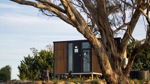 Un edificio moderno con fachada de madera, una puerta de cristal y un pequeño espacio exterior con mesas y sillas.
