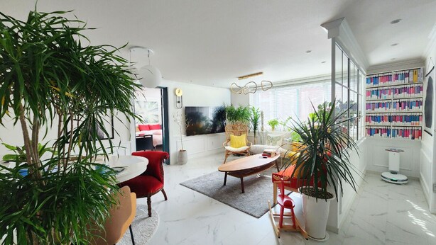 Un salon moderne avec une grande plante en pot, un fauteuil rouge, une table basse en bois et une bibliothèque remplie de livres.