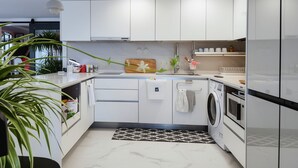 Une cuisine moderne avec des meubles blancs, un lave-linge et un plan de travail sur lequel sont disposés divers objets.