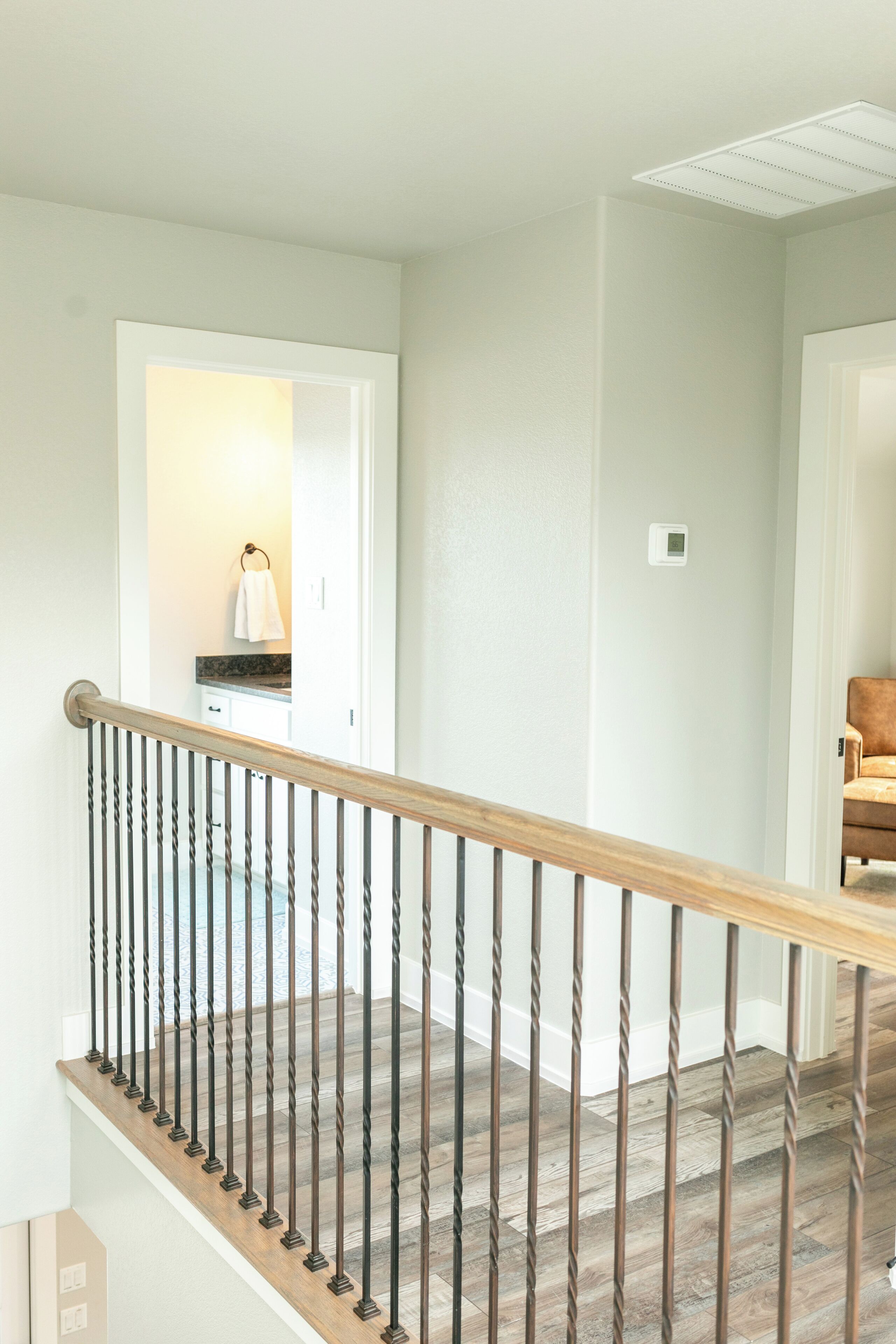 Un escalier avec une main courante en bois et des balustrades en métal, menant à une pièce dotée d’une porte blanche et d’une salle de bain visible, où une serviette est accrochée au mur.