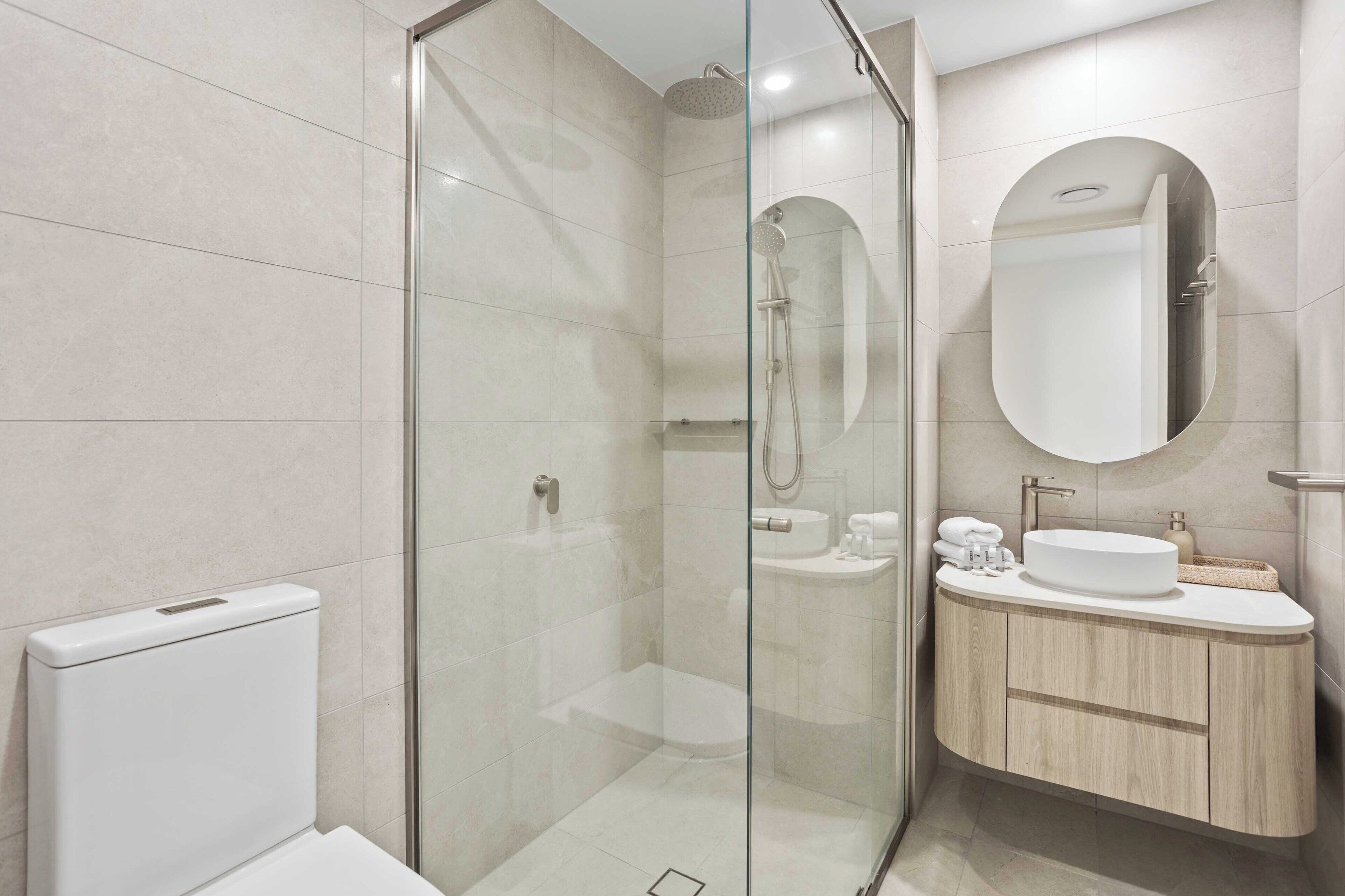 A modern bathroom with a glass-enclosed shower, a toilet, and a vanity with a sink and mirror.