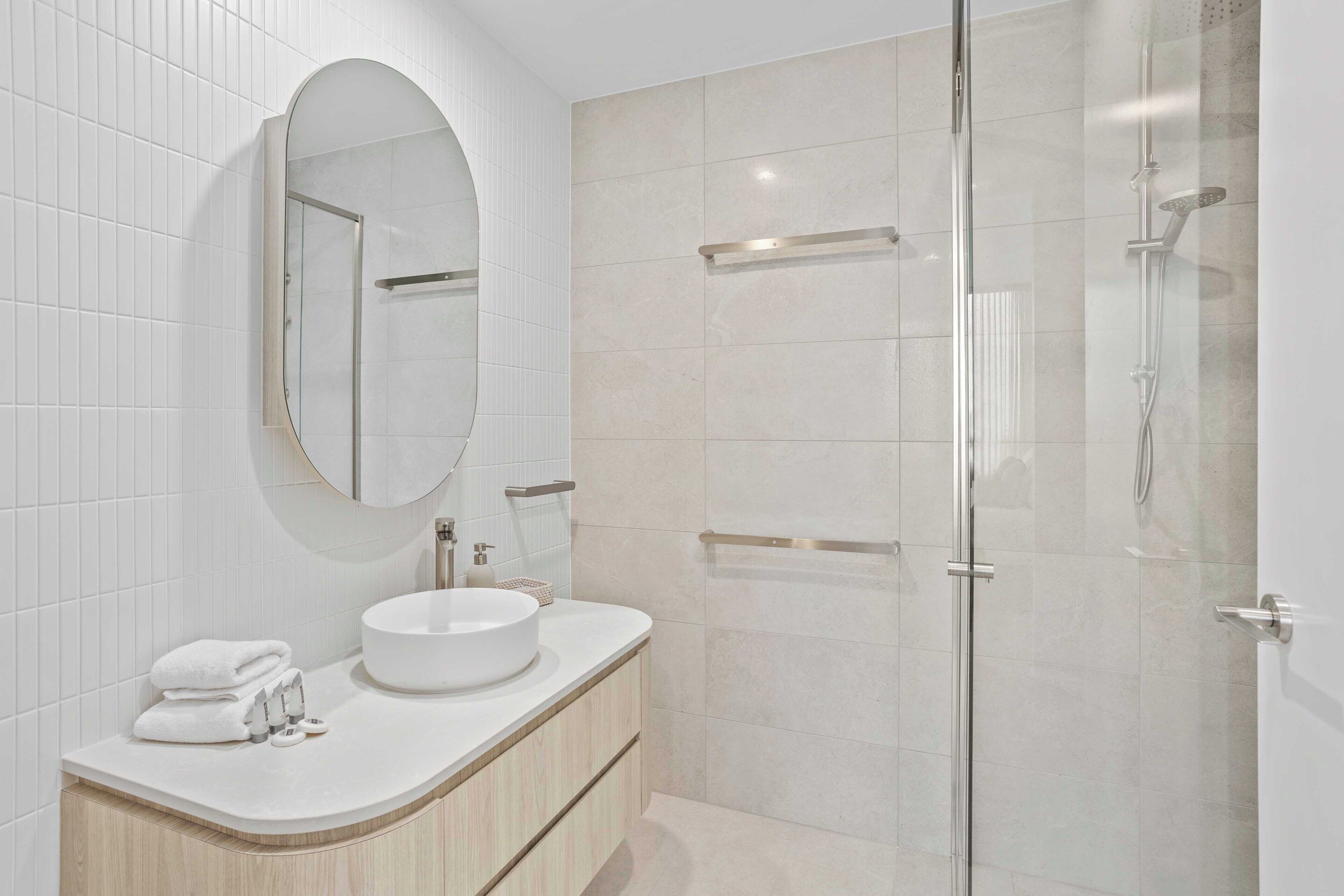 A modern bathroom with a round mirror, a white sink, and a glass-enclosed shower.