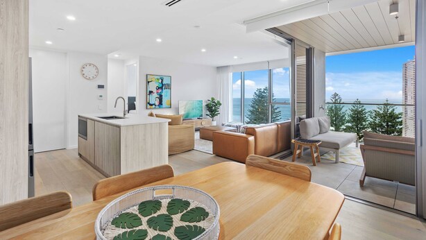 A modern living space with a dining area, kitchen, and a balcony with a view. - Luxury Ocean View Burleigh Apartment (Burleigh Heads)