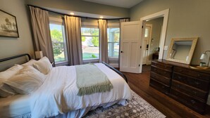 Quarto com cama, cômoda, espelho e janela com cortinas.