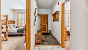 A hallway leading to a bedroom with a bed, wooden furniture, and a door. - Mountain Escape | Hot Tub + Walk to Town (Breckenridge)